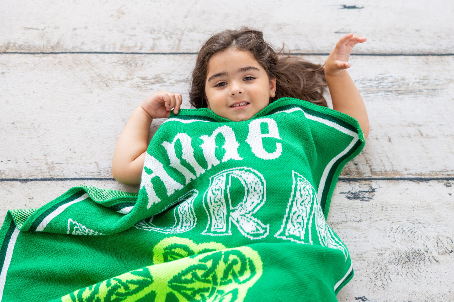 Child holding a green towel with white text on a wooden floor