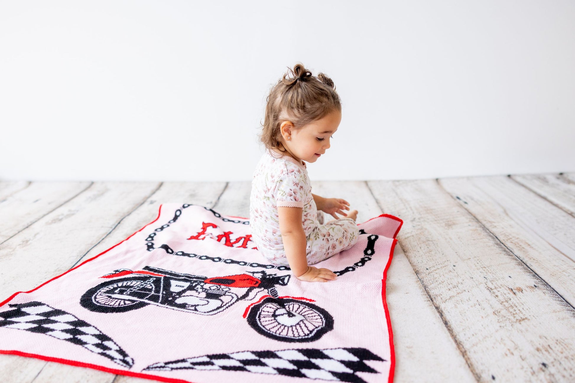 Child sitting on a motorcycle-themed blanket on a wooden floor