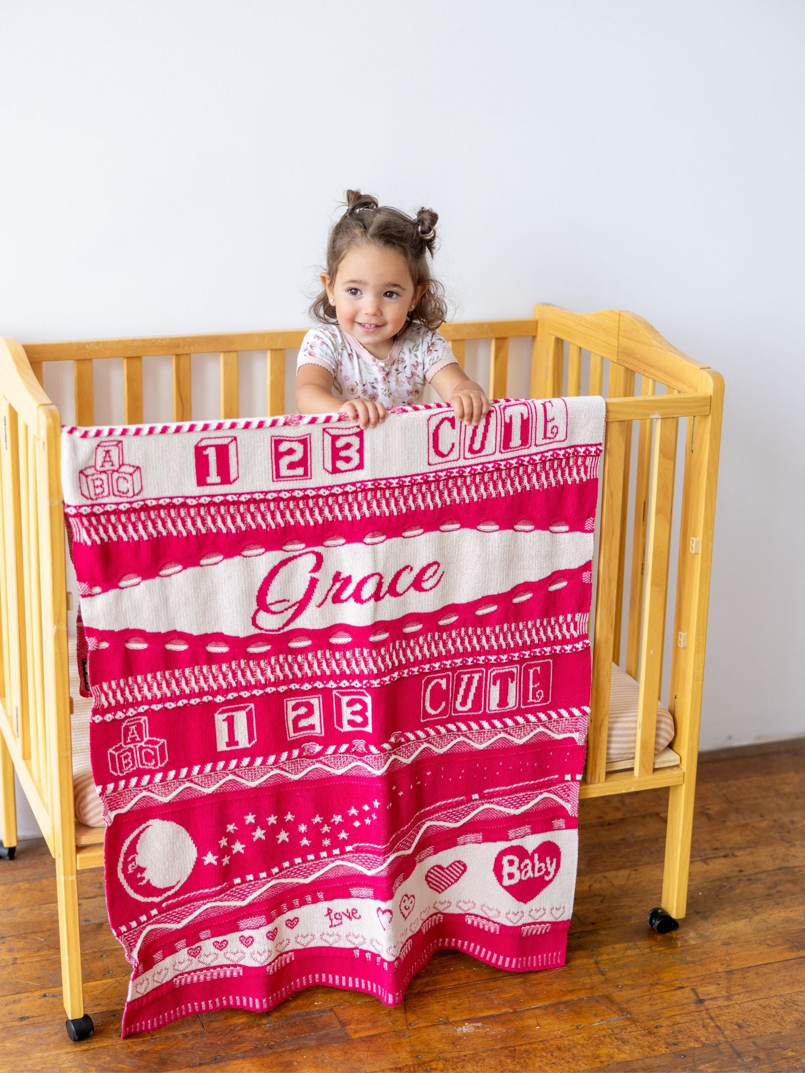 Child holding a pink and white blanket with text in a crib