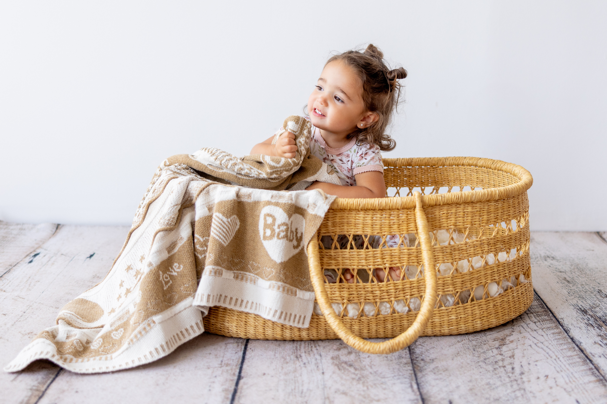 Child sitting inside a wicker Moses basket with a baby blanket.