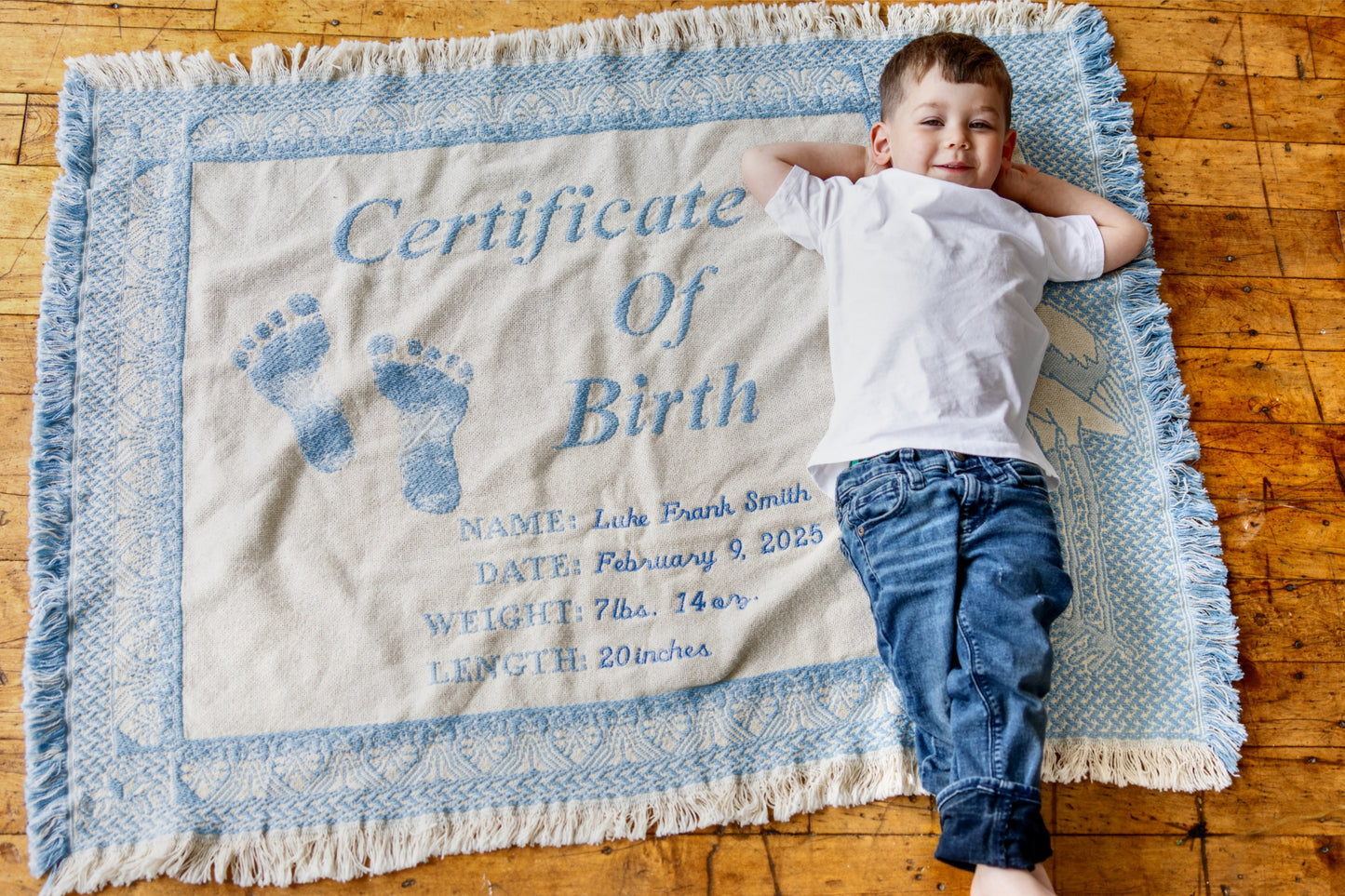 Child lying on a blanket with a 'Certificate of Birth' print on a wooden floor