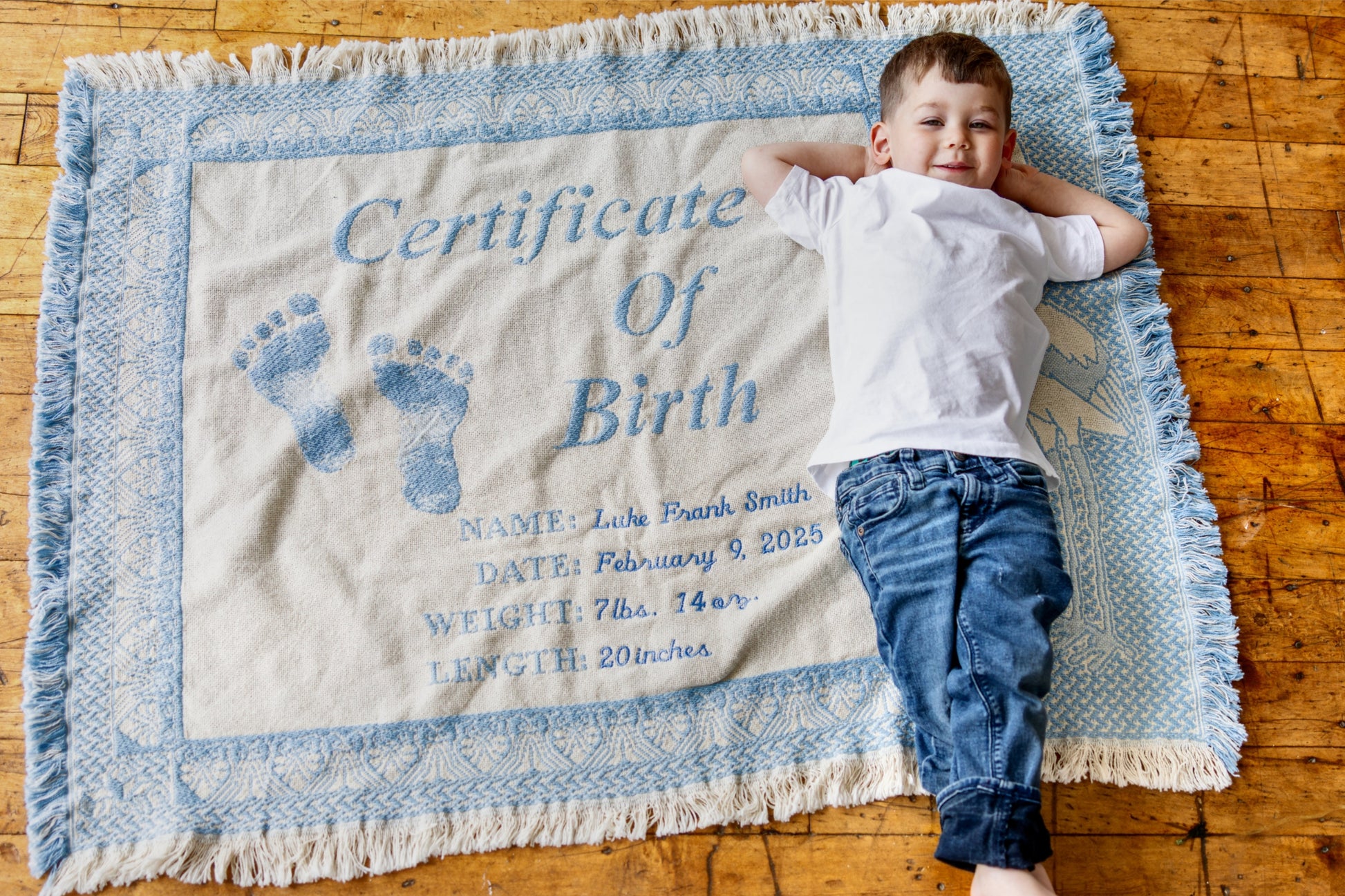 Child lying on a blanket with a 'Certificate of Birth' print on a wooden floor