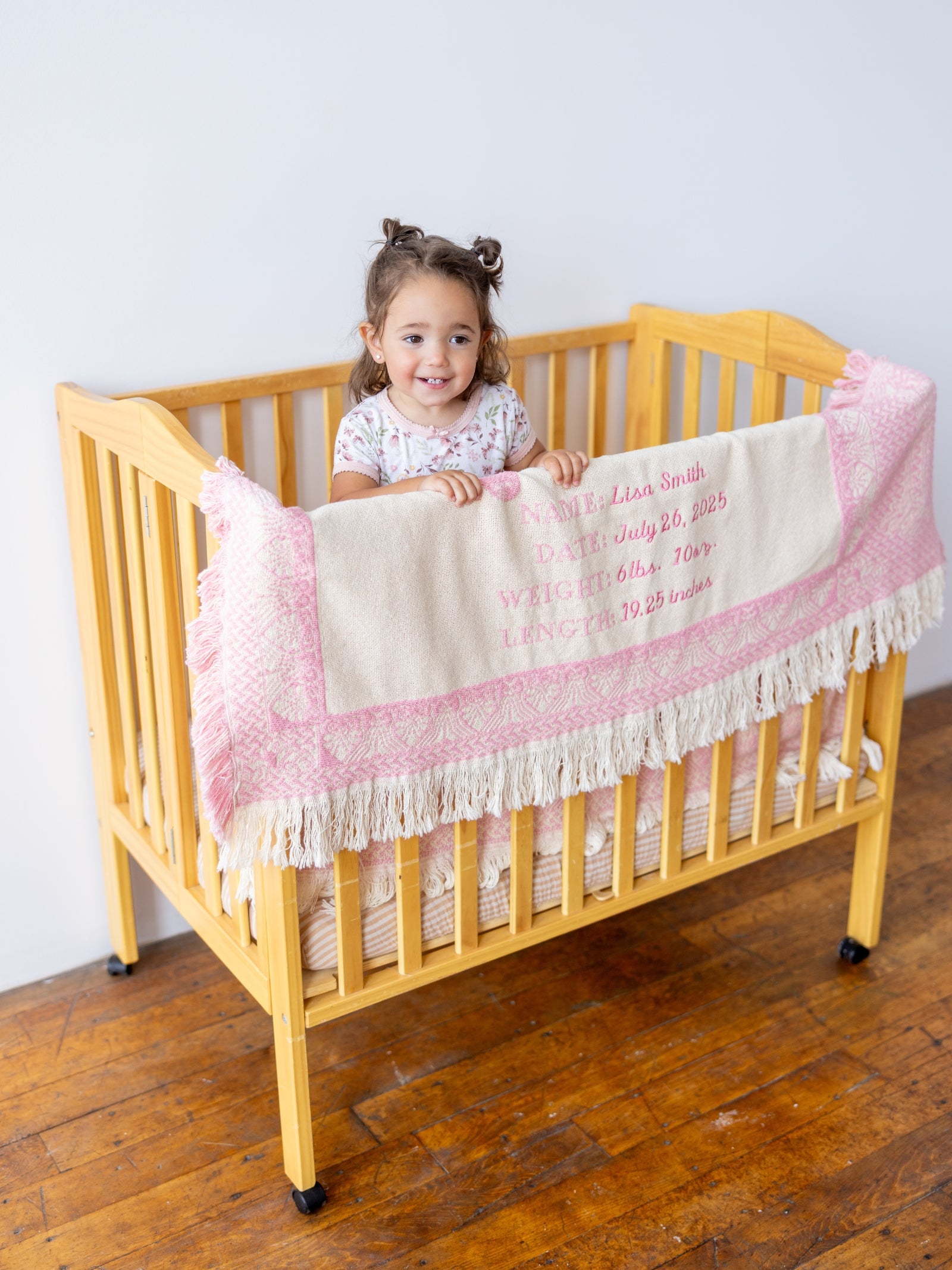 Child standing in a crib with a pink and white blanket, smiling.